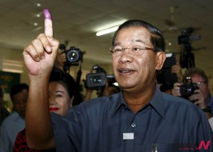 Cambodia's Prime Minister Hun Sen, foreground, shows off his inked finger at a polling station in Takhmau town, south of Phnom Penh, Cambodia, Sunday, July 28, 2013. Cambodians began voting across the country Sunday to take part in what has become a familiar ritual - the re-election of Prime Minister Hun Sen, who has been on the job for 28 years and says he hopes to rule for at least another decade. (AP Photo/Heng Sinith)