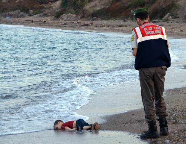 A paramilitary police officer investigates the scene before carrying the lifeless body of Aylan Kurdi, 3, after a number of migrants died and a smaller number were reported missing after boats carrying them to the Greek island of Kos capsized, near the Turkish resort of Bodrum early Wednesday, Sept. 2, 2015. The tides also washed up the bodies of Rehan and Galip on Turkey's Bodrum peninsula Wednesday, Abdullah survived the tragedy. (AP Photo/DHA)