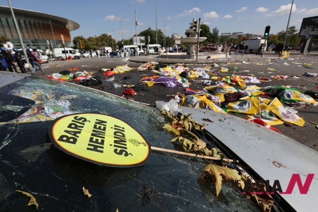 A placard that reads in Turkish: 'Peace Immediately Now' , is seen at the site of an explosion with the bodies of victims covered with flags and banners in the background,  in Ankara, Turkey, Saturday, Oct. 10, 2015. The two bomb explosions targeting a peace rally in the capital Ankara has killed dozens of people and injured scores of others. The explosions occurred minutes apart near Ankara's main train station as people were gathering for the rally, organized by the country's public sector workers' trade union and other civic society groups. The rally aimed to call for an end to the renewed violence between Kurdish rebels and Turkish security forces.  (AP Photo/Burhan Ozbilici)