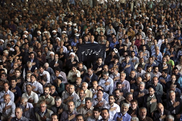 Iranian mourners attend the funeral ceremony of some pilgrims who were killed in a stampede during the hajj pilgrimage in Saudi Arabia last month, as a mourner holds a banner which reads in Arabic, "May Allah Curse Al-Saud," referring to Saudi Arabia's ruling family, at Tehran University, in Tehran, Iran. (AP Photo/Vahid Salemi)  